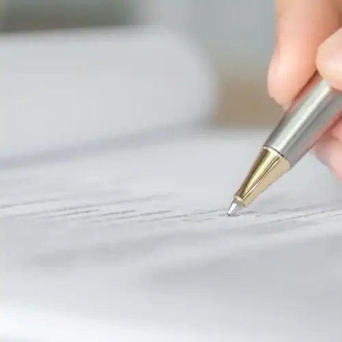 Mano firmando un documento con un bolígrafo plateado