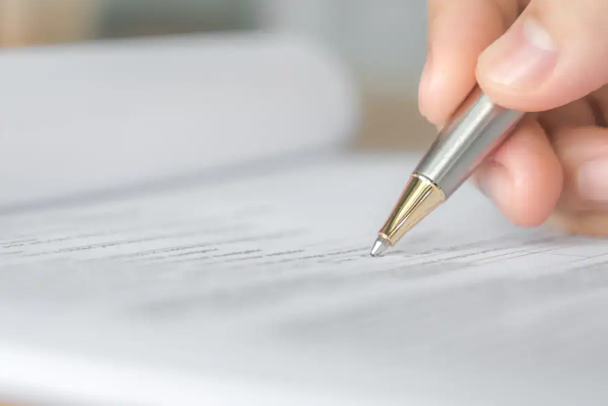 Mano firmando un documento con un bolígrafo plateado